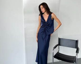 May include: A navy blue satin top with a V-neck and a drawstring detail. The top is paired with a matching navy blue satin skirt.
