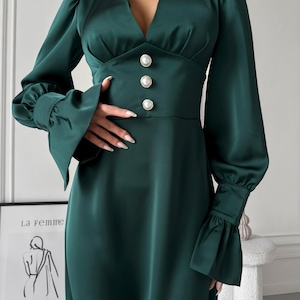 May include: A long-sleeved, emerald green satin dress with a V-neckline and pearl button accents. The dress has a fitted bodice and a flowing skirt.