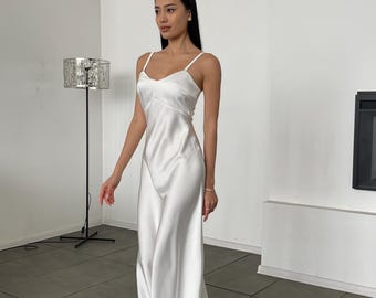 May include: A white satin slip dress with thin straps. The dress has a simple, elegant design and falls to the ankles.