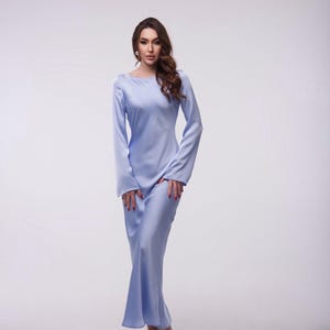 May include: A woman wearing a light blue satin maxi dress with long sleeves and a scoop neckline. She is standing on a white background.