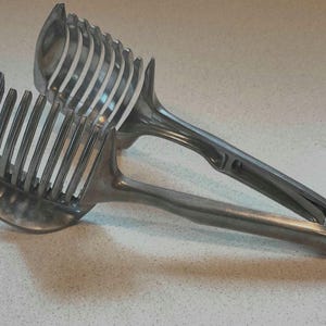 May include: A silver metal citrus fruit cutter with a handle and a series of blades for slicing fruit.