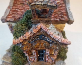 May include: A miniature schoolhouse figurine with a brick facade, a brown wooden door, and a bell tower. The schoolhouse is labeled "Boyd's School" and is surrounded by green foliage.
