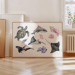 Può includere: Stampa incorniciata con illustrazioni ad acquerello di varie creature marine, tra cui una tartaruga, uno squalo e razze. L'opera d'arte include conchiglie e un pesce colorato, tutti adornati con fiocchi rosa. Lo sfondo è beige neutro.