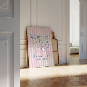 May include: A pink and white striped poster with a blue line drawing of two bikini tops hanging on a clothesline. The text "dolce far niente" is written in blue below the bikini tops.