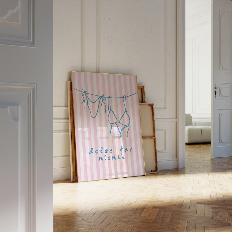 May include: A pink and white striped poster with a blue line drawing of two bikini tops hanging on a clothesline. The text "dolce far niente" is written in blue below the bikini tops.