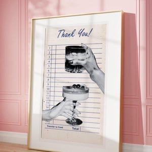 May include: A framed print featuring a vintage-style receipt with the words "Thank You!" in blue script. The image shows two hands holding cocktails, one a rocks glass and the other a coupe glass with cherries. The frame is gold.