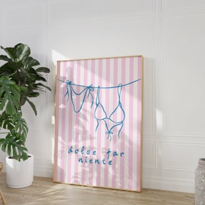 May include: A pink and white striped poster with a blue line drawing of two swimsuits hanging on a clothesline. The text "dolce far niente" is written in blue below the swimsuits.