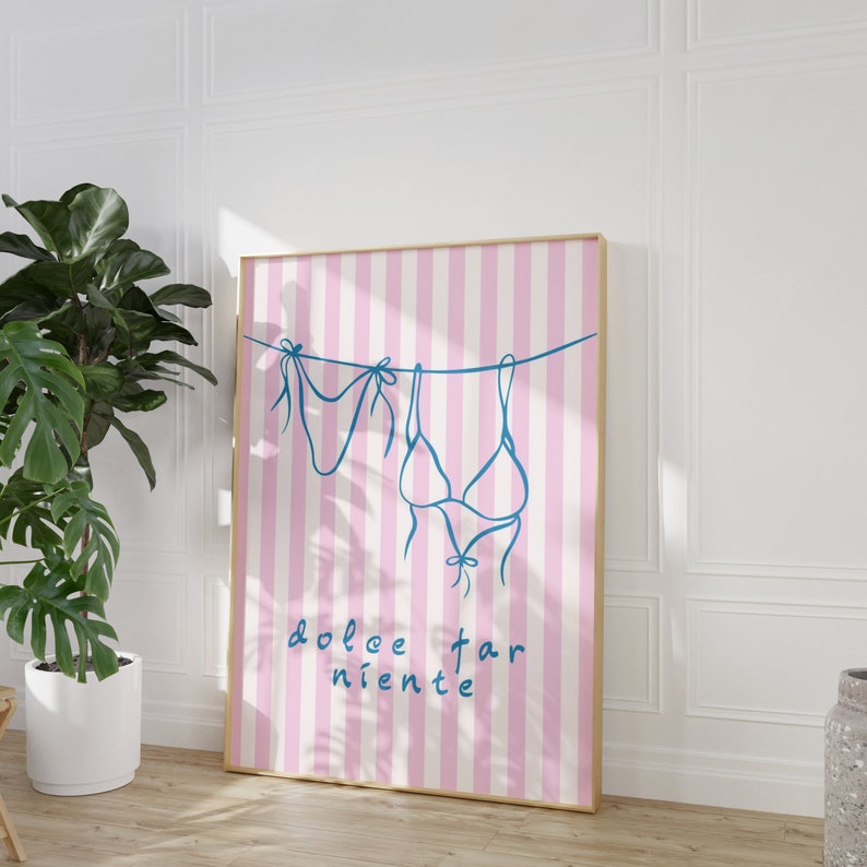 May include: A pink and white striped poster with a blue line drawing of two swimsuits hanging on a clothesline. The text "dolce far niente" is written in blue below the swimsuits.
