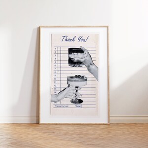 May include: A framed print featuring a vintage-style receipt with the words "Thank You!" in blue script. Two hands are holding cocktails, one a rocks glass and the other a coupe glass. The print is in a gold frame.