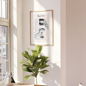 May include: A framed print featuring a vintage-style receipt with the words "Thank You!" at the top. The receipt shows illustrations of two cocktails being held by hands. The frame is gold-colored.