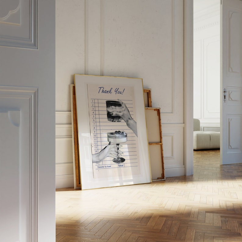May include: A framed print with a gold border leans against a white wall. The print features a vintage-style receipt with illustrations of cocktails and the text "Thank You!". The image is in black and white with blue lines.