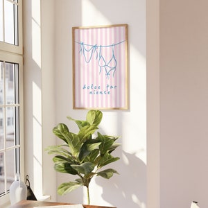 May include: A framed print with a pink and white striped background. Two blue bikini tops are hanging on a line with the text "dolce far niente" below.