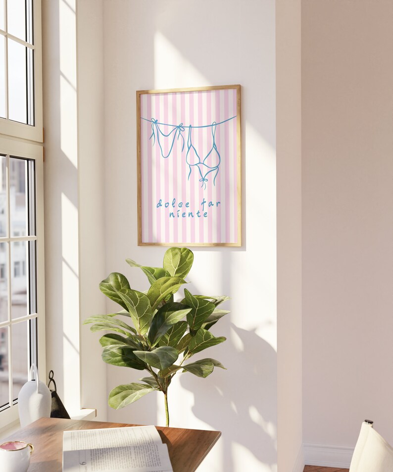 May include: A framed print with a pink and white striped background. Two blue bikini tops are hanging on a line with the text "dolce far niente" below.