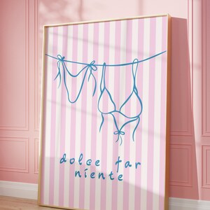 May include: A pink and white striped poster with a blue outline of a bikini hanging on a clothesline. The text "dolce far niente" is written in cursive at the bottom of the poster.