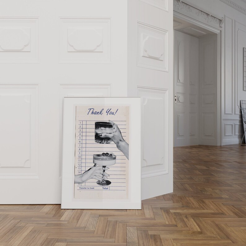 May include: A framed print featuring a vintage-style receipt with the words "Thank You!" in blue script. The image depicts hands holding a cocktail and a stemmed glass with cherries. The print is displayed against a white wall and wooden floor.