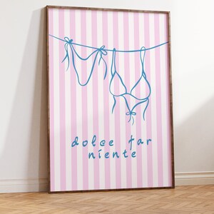 May include: A framed print with a pink and white striped background. The print features a blue line drawing of a bikini top and bottom hanging on a clothesline. The text "dolce far niente" is written in blue below the bikini.
