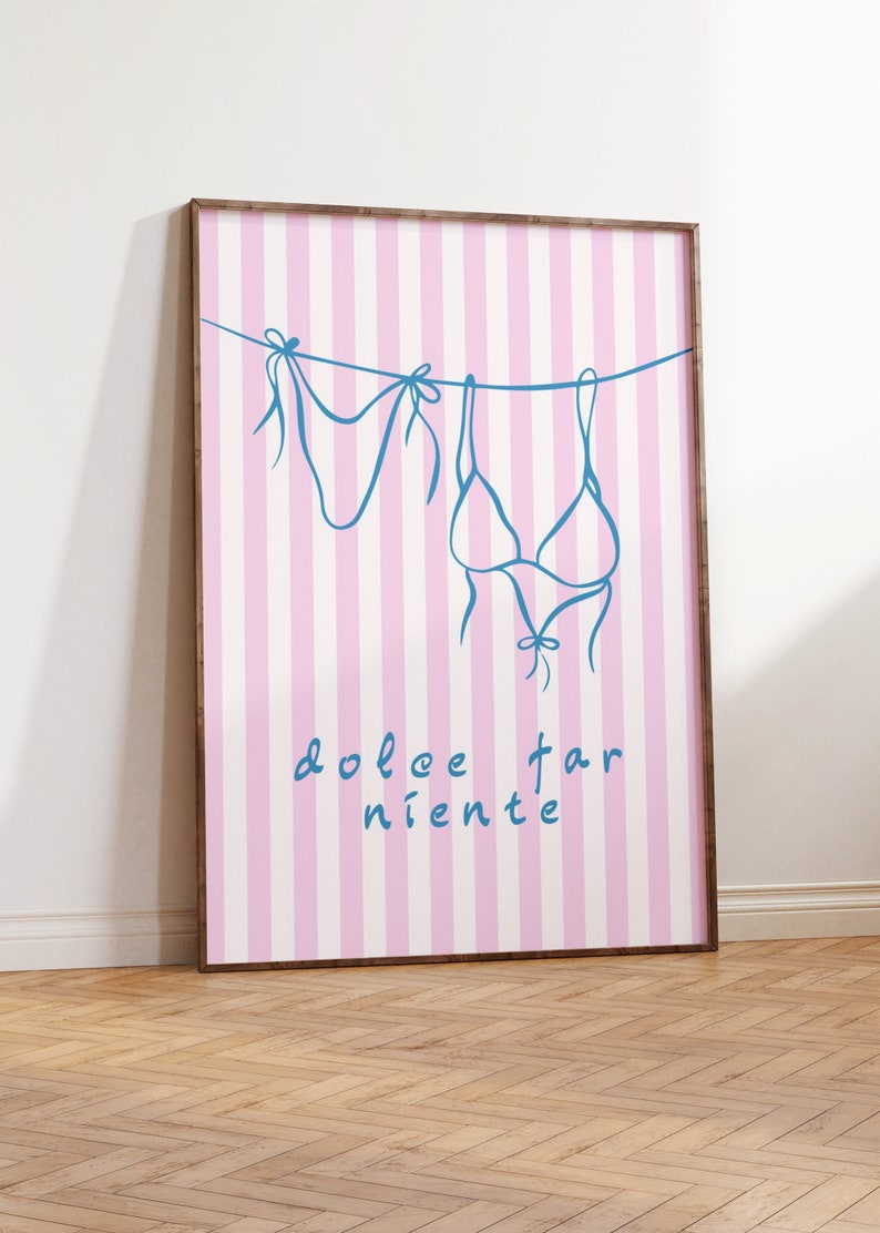 May include: A framed print with a pink and white striped background. The print features a blue line drawing of a bikini top and bottom hanging on a clothesline. The text "dolce far niente" is written in blue below the bikini.