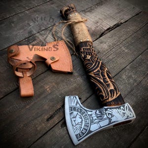 Puede incluir: Un hacha vikinga hecha a mano con un mango de madera negro y marr&oacute;n con intrincados tallados. La cabeza del hacha est&aacute; hecha de acero y tiene un acabado plateado con un s&iacute;mbolo vikingo y runas grabadas en ella. El hacha viene con una funda de cuero marr&oacute;n.