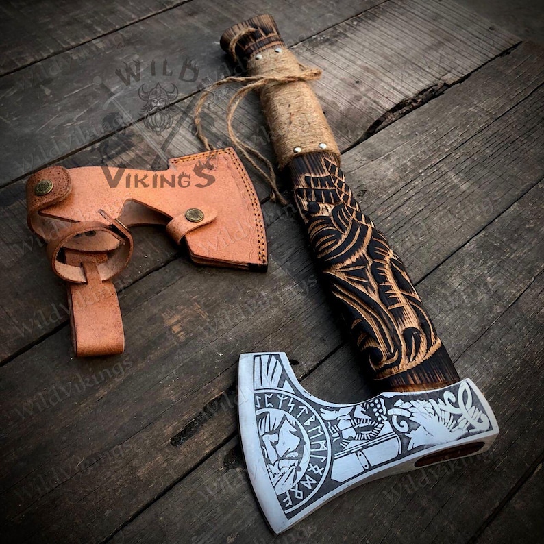 Puede incluir: Un hacha vikinga hecha a mano con un mango de madera negro y marr&oacute;n con intrincados tallados. La cabeza del hacha est&aacute; hecha de acero y tiene un acabado plateado con un s&iacute;mbolo vikingo y runas grabadas en ella. El hacha viene con una funda de cuero marr&oacute;n.