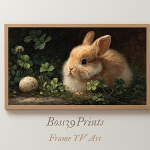 May include: A framed print featuring a fluffy brown rabbit nestled among green clover and grass, with a speckled egg nearby. The artwork has a vintage aesthetic, with soft lighting and a dark background. The frame is a light brown color. The text "Boss39 Prints Frame TV Art" is at the bottom.