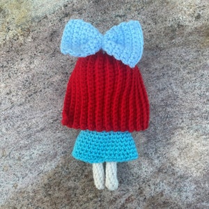May include: A crocheted doll with red hair, a blue bow, a blue skirt, and white legs.