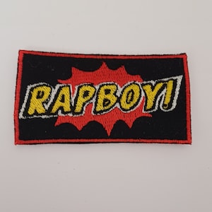May include: A black and red embroidered patch with the word "RAPBOY!" in yellow letters with white outlines.