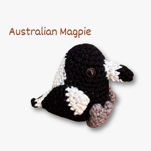 May include: A crocheted Australian Magpie bird in black, white, and grey. The bird has a large black eye and is labelled "Australian Magpie" in brown text.