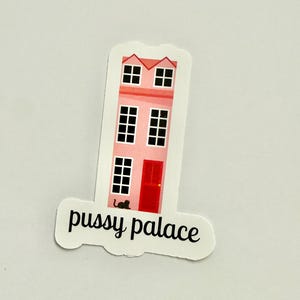 May include: A sticker featuring a pink house with a red door and black windows. The text "pussy palace" is written in black cursive font below the house. A black cat is near the door.