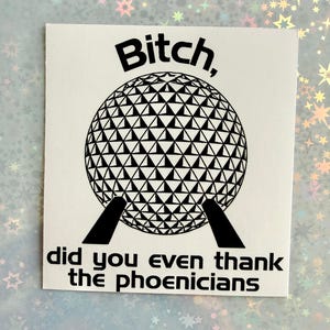 May include: A square white sticker featuring a black graphic of a geodesic dome structure. Above the dome, the text reads "Bitch," and below the dome, the text reads "did you even thank the phoenicians" in a bold, sans-serif black font.