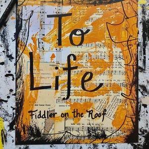 May include: Mixed media artwork with the words "To Life" and "Fiddler on the Roof" in black lettering. The background features sheet music and orange paint splatters, framed by a black border.