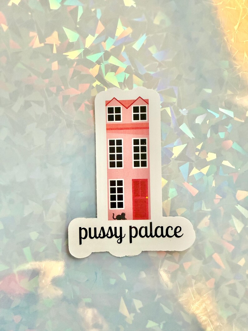 May include: A sticker featuring a pink building with black windows and a red door. The text "pussy palace" is written in black script below the building. A small black cat is near the door.
