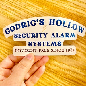 May include: White sticker with blue text that reads "Godric's Hollow Security Alarm Systems Incident Free Since 1981". A lightning bolt symbol is between "Godric's" and "Hollow".