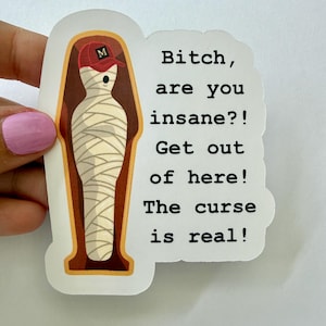 May include: A die-cut sticker featuring a mummy wearing a red baseball cap with a letter M, lying inside a brown coffin. The text reads: Bitch, are you insane?! Get out of here! The curse is real! The sticker has a white border and a matte finish.