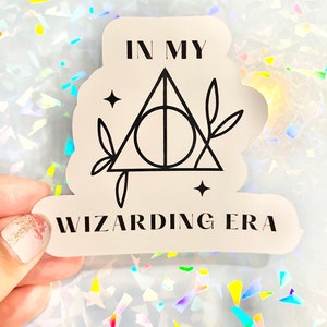 May include: A white sticker with black text and a black graphic of the Deathly Hallows symbol. The text reads "In My Wizarding Era".