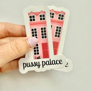 May include: Pink house stickers with black windows, red doors, and a black cat silhouette. The stickers have the words "pussy palace" in black script.