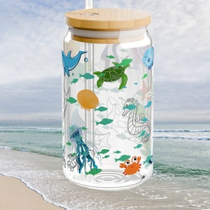 May include: A clear glass tumbler with a bamboo lid and a glass straw, featuring a colorful wrap-around print of various sea creatures including a green sea turtle, orange crab, blue dolphin, jellyfish, seahorse, and small teal fish.