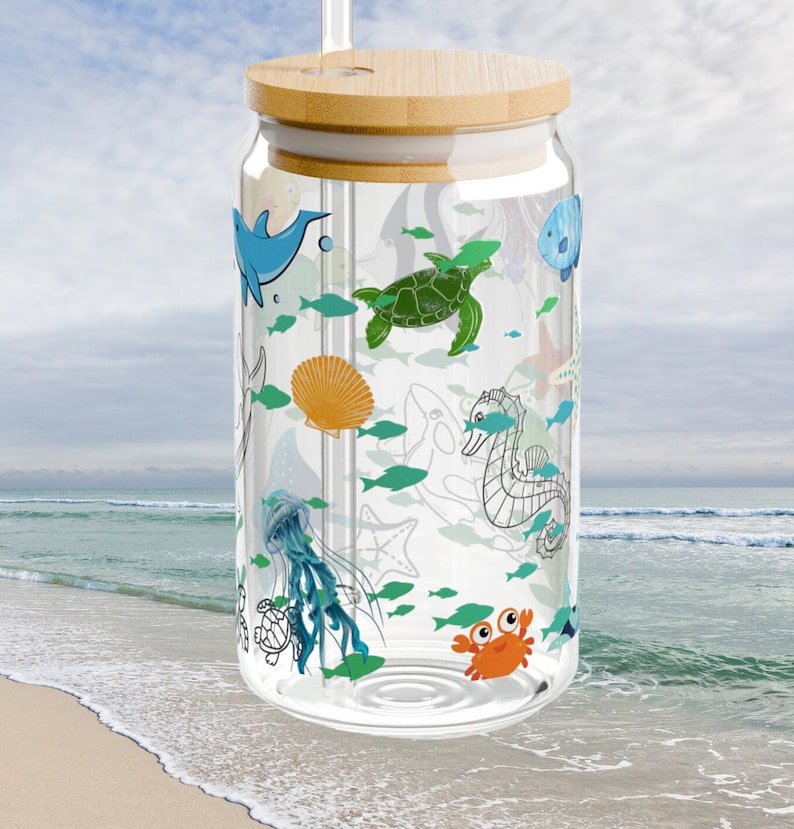 May include: A clear glass tumbler with a bamboo lid and a glass straw, featuring a colorful wrap-around print of various sea creatures including a green sea turtle, orange crab, blue dolphin, jellyfish, seahorse, and small teal fish.