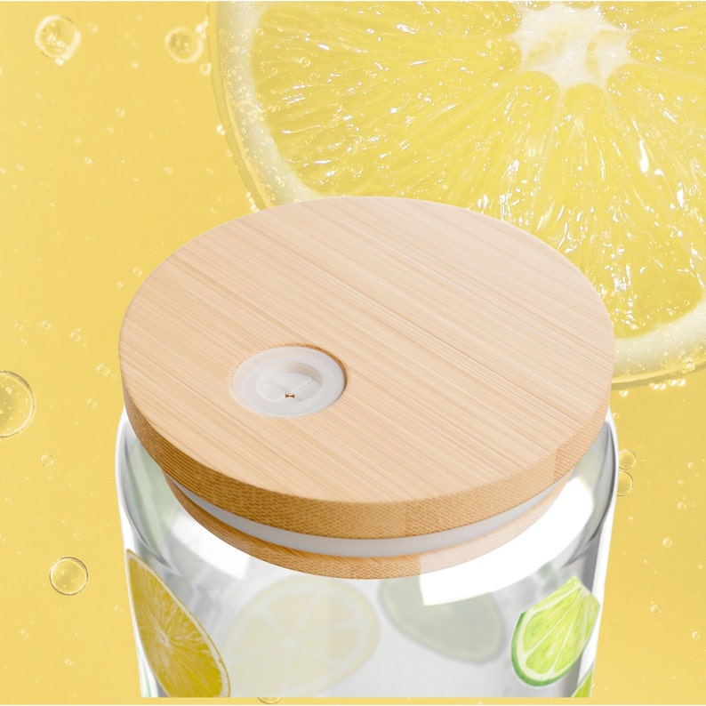 May include: A clear glass tumbler featuring a pattern of yellow lemon and green lime slices. The container is topped with a round, light-colored bamboo lid that includes a small, circular white silicone insert with a central straw opening.