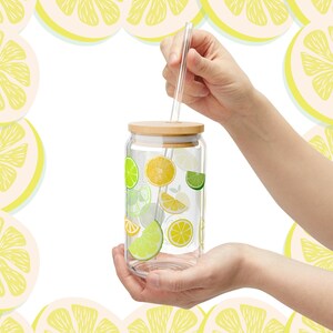 May include: A clear glass tumbler with a bamboo lid and a glass straw, featuring a colorful pattern of yellow lemon and green lime slices printed on the exterior. The cylindrical glass container is designed for beverages and includes a straw hole.