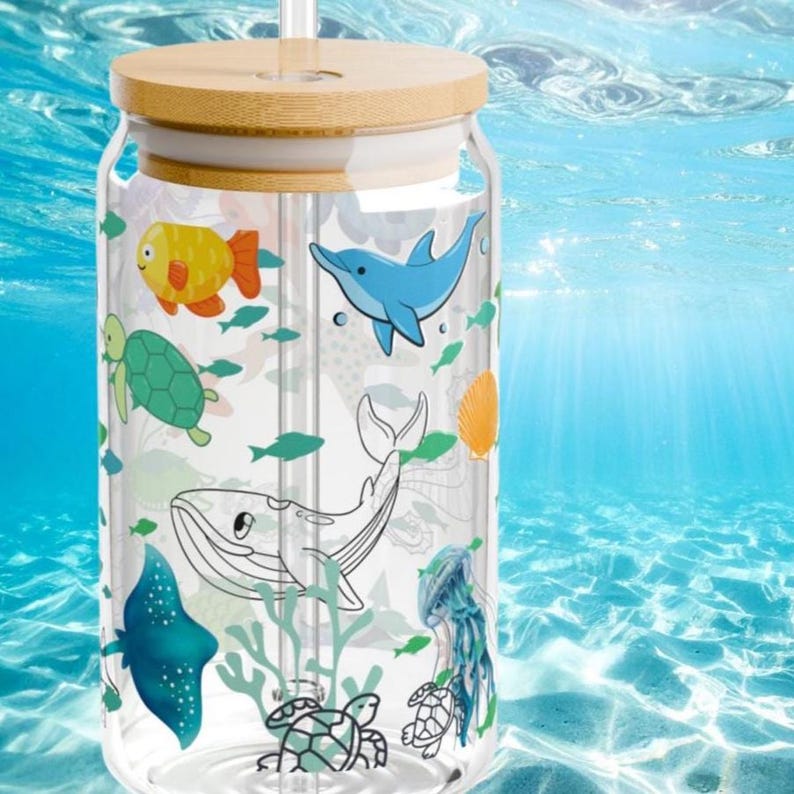 May include: A clear glass tumbler with a bamboo lid and a glass straw, featuring a colorful pattern of various sea creatures including a yellow fish, a blue dolphin, a green turtle, a whale, a stingray, and a jellyfish against a clear background.