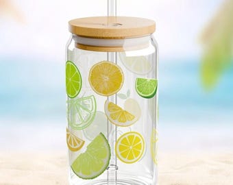 May include: A clear glass tumbler with a bamboo lid and a glass straw, featuring a colorful pattern of yellow lemon slices and green lime slices printed on the exterior. The cylindrical glass has a wide mouth and a flat base for stability.