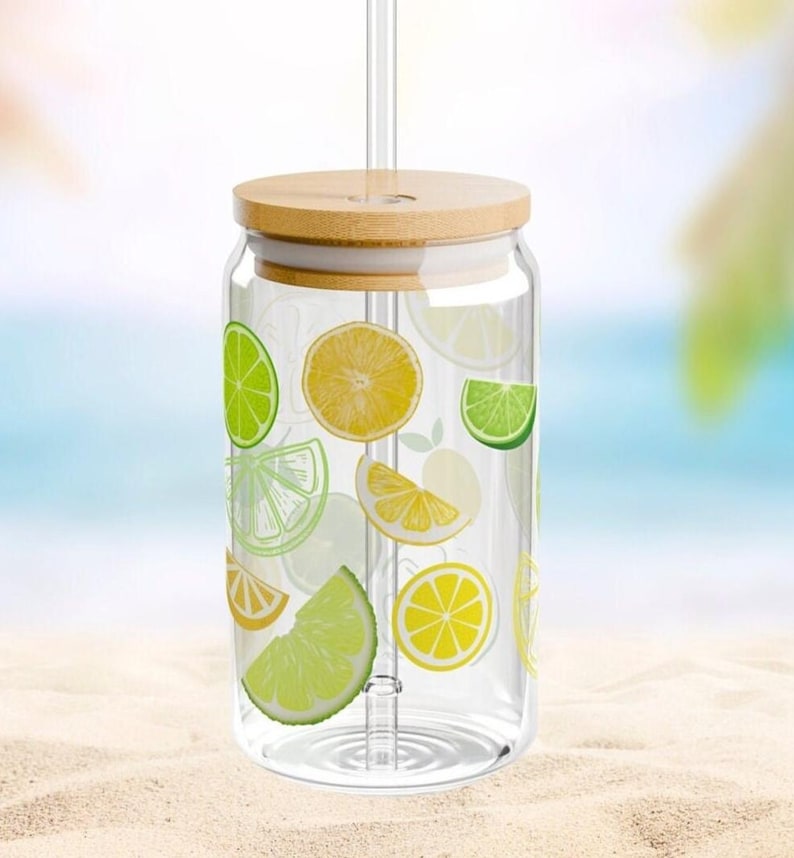 May include: A clear glass tumbler with a bamboo lid and a glass straw, featuring a colorful pattern of yellow lemon slices and green lime slices printed on the exterior. The cylindrical glass has a wide mouth and a flat base for stability.