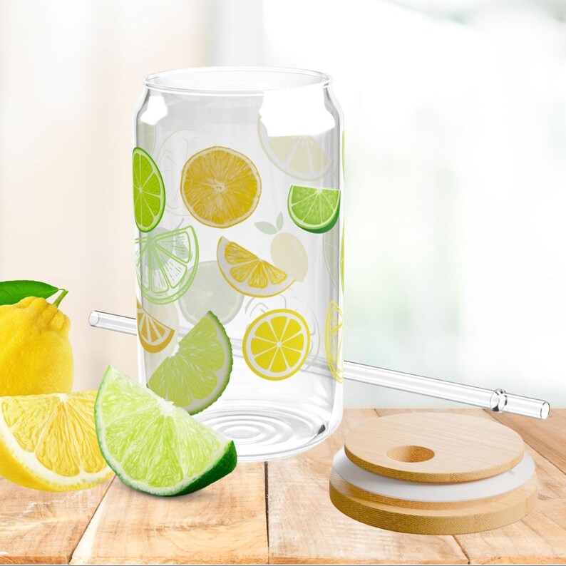 May include: A clear glass tumbler shaped like a soda can, decorated with a pattern of yellow lemon and green lime slices. The set includes a matching clear glass straw and a round, light-colored wooden lid with a circular opening for the straw.