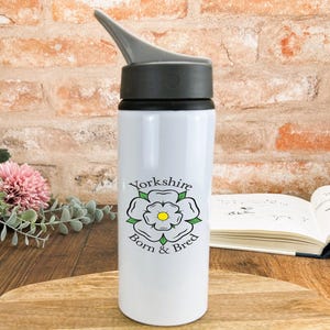 May include: White water bottle with a black lid and a white rose with green leaves and the text "Yorkshire Born & Bred".