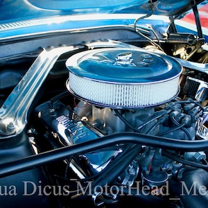 Puede incluir: Vista de cerca de un motor de coche clásico con un filtro de aire cromado y varios manguitos y cables. El motor está en un compartimento del motor azul.