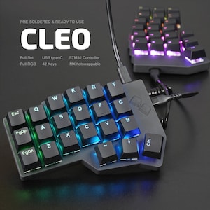 Könnte beinhalten: Schwarze CLEO-Tastatur mit 42 Tasten, vorverdrahtet und einsatzbereit. Die Tastatur verfügt über eine vollständige RGB-Hintergrundbeleuchtung und einen USB-Typ-C-Anschluss. Die Tasten sind mit einem Farbverlauf aus Blau, Grün und Lila beleuchtet.