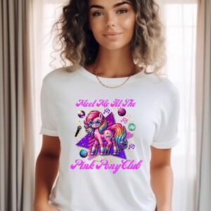 May include: White t-shirt with a pink, purple, and rainbow cartoon pony wearing sunglasses and holding a microphone. The text "Meet Me At The Pink Pony Club" is printed on the shirt.