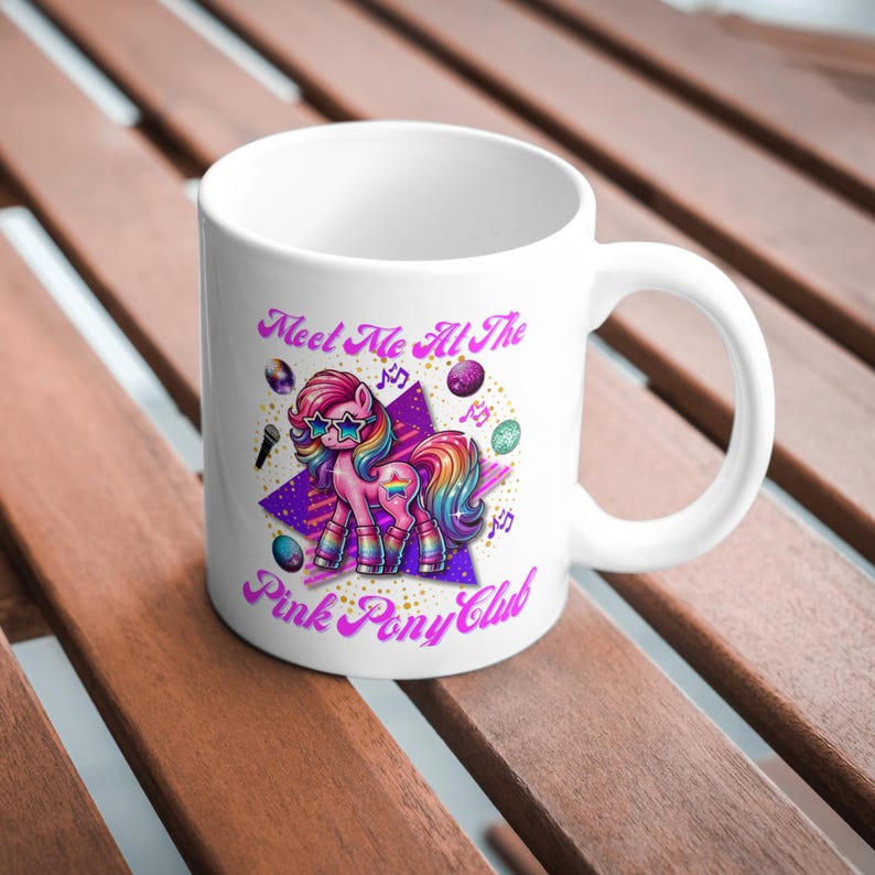 May include: White ceramic mug with a pink pony wearing sunglasses and roller skates. The mug has the text "Meet Me At The Pink Pony Club" in pink and purple lettering.