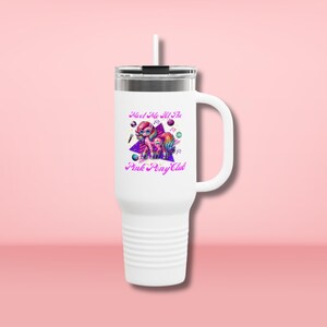 May include: White stainless steel travel mug with a handle and a straw. The mug has a pink and purple graphic of two cartoon ponies with the text "Meet Me At The Pink Pony Club".