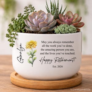 May include: A white ceramic planter with a variety of succulents and a wooden saucer. The planter has a floral illustration and text that reads "May you always remember...Happy Retirement! Est. 2026."